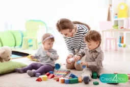 Jovem Au Pair brincando com duas crianças pequenas em uma sala colorida.