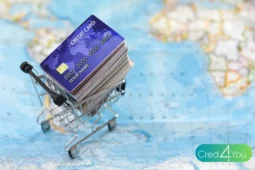 Carrinho de compras com vários cartões de crédito sobre um mapa-múndi, simbolizando os cartões que dão acesso a sala VIP e benefícios de viagem internacional.