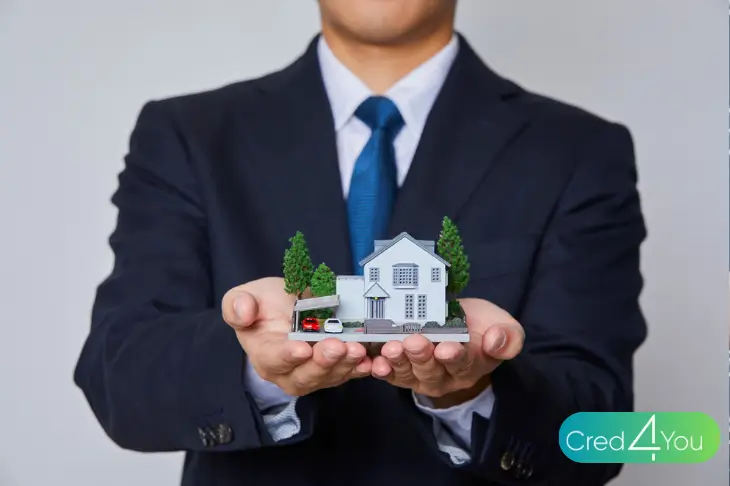 Homem de terno segurando miniatura de casa, representando a conquista do imóvel por meio do consórcio imobiliário.