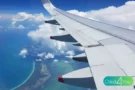 Vista aérea da asa de um avião sobre o mar azul, simbolizando como acumular milhas pode aproximar o viajante do próximo destino.