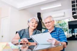 Älteres Paar liest Dokument am Tisch, Symbol für Entscheidung Riester-Rente oder Rürup-Rente.