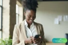 Mulher sorrindo usando o celular em um escritório, conceito de conta salário.